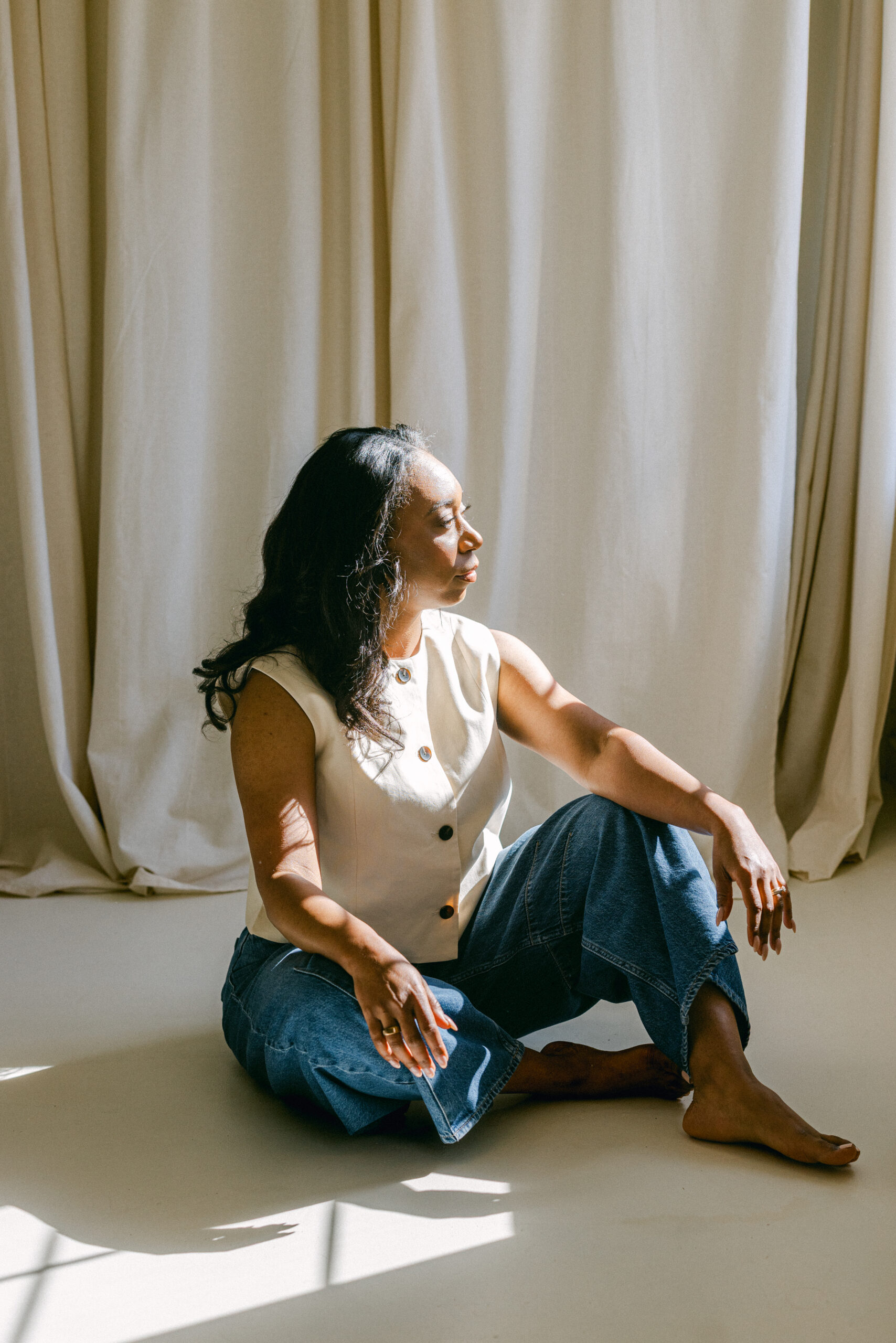a girl sitting in front of white curtains looking at the window during her brand photography session