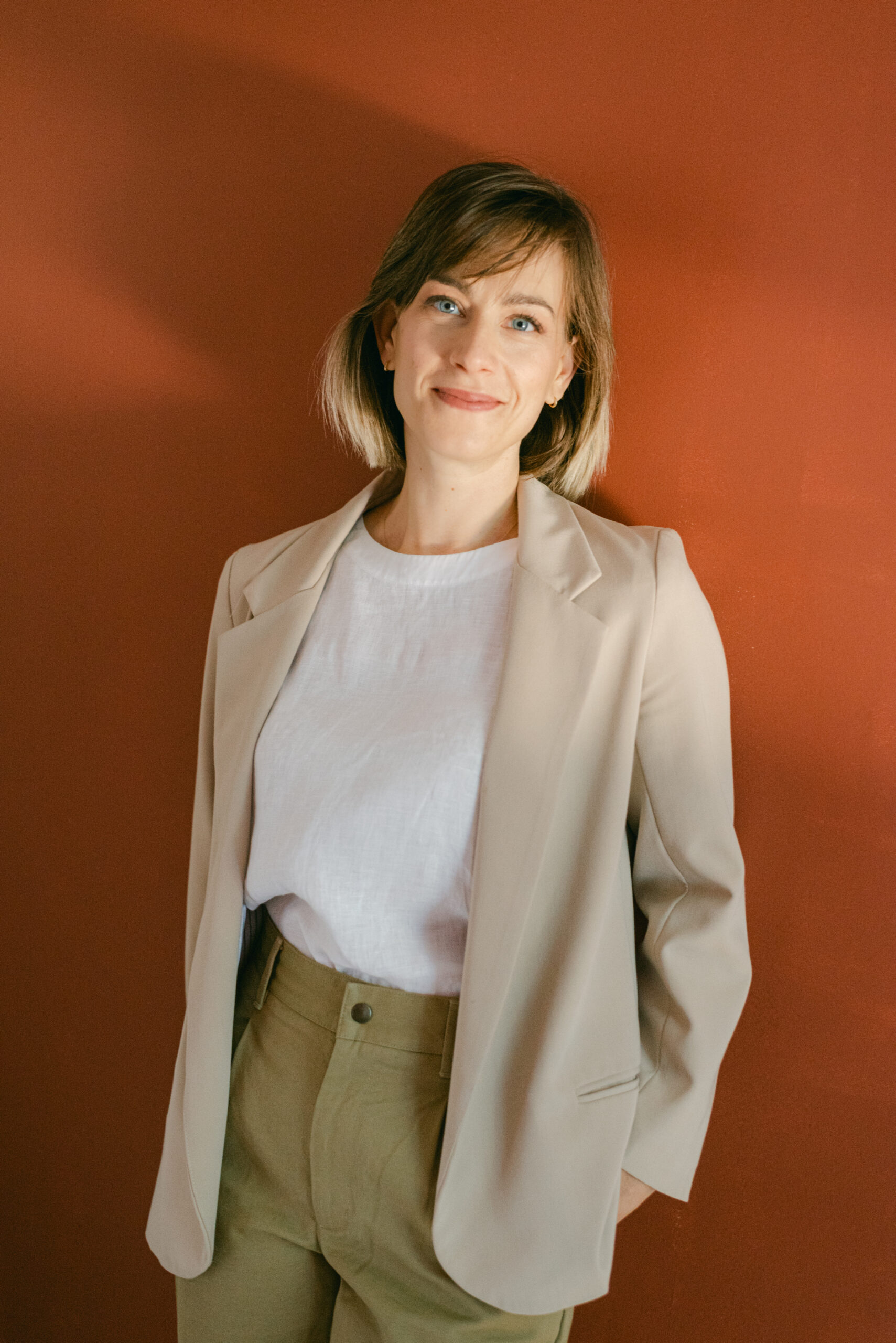 a woman standing in front of a red wall wearing a suit jacket