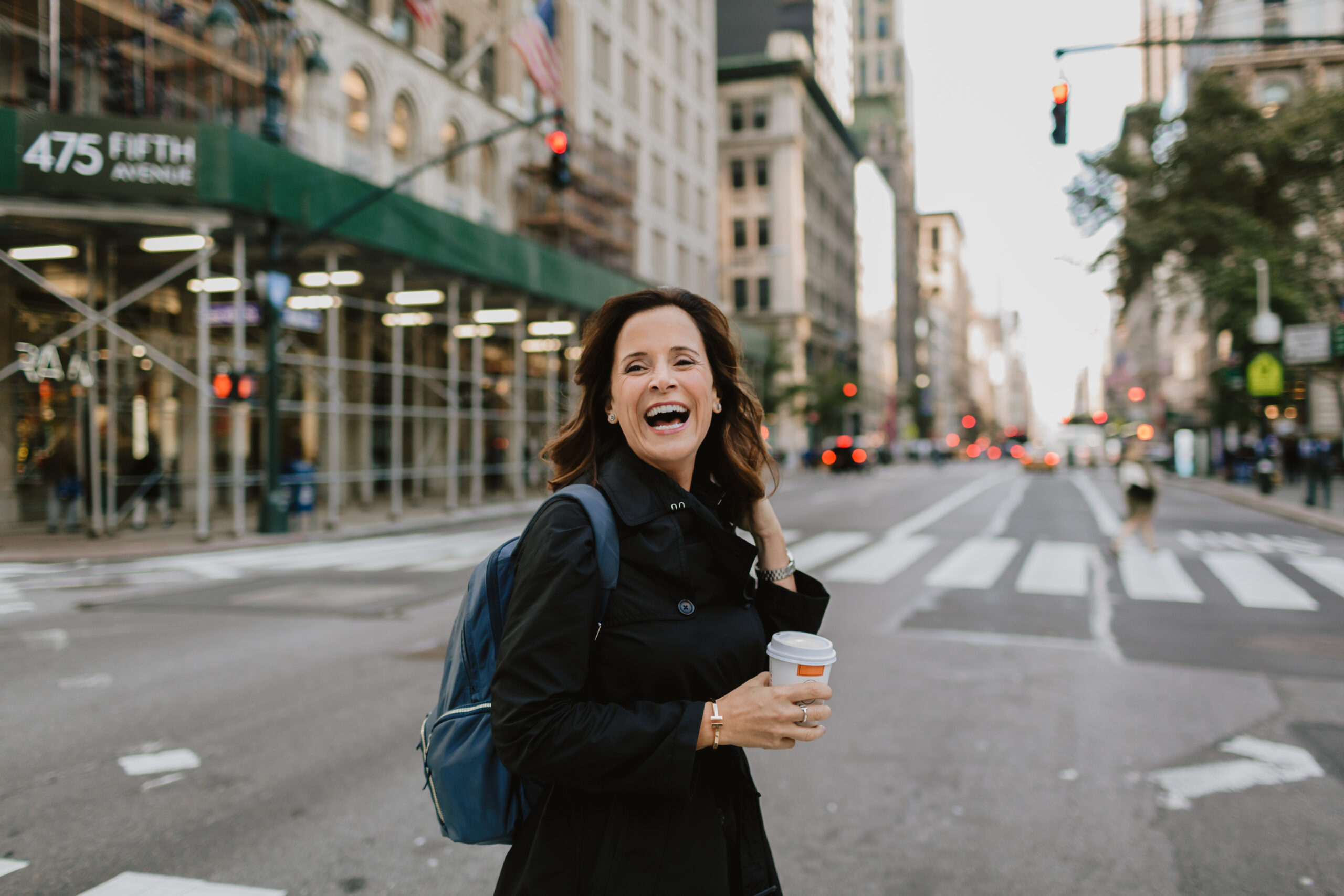 a woman walking with a coffee cup across the street in NYC
