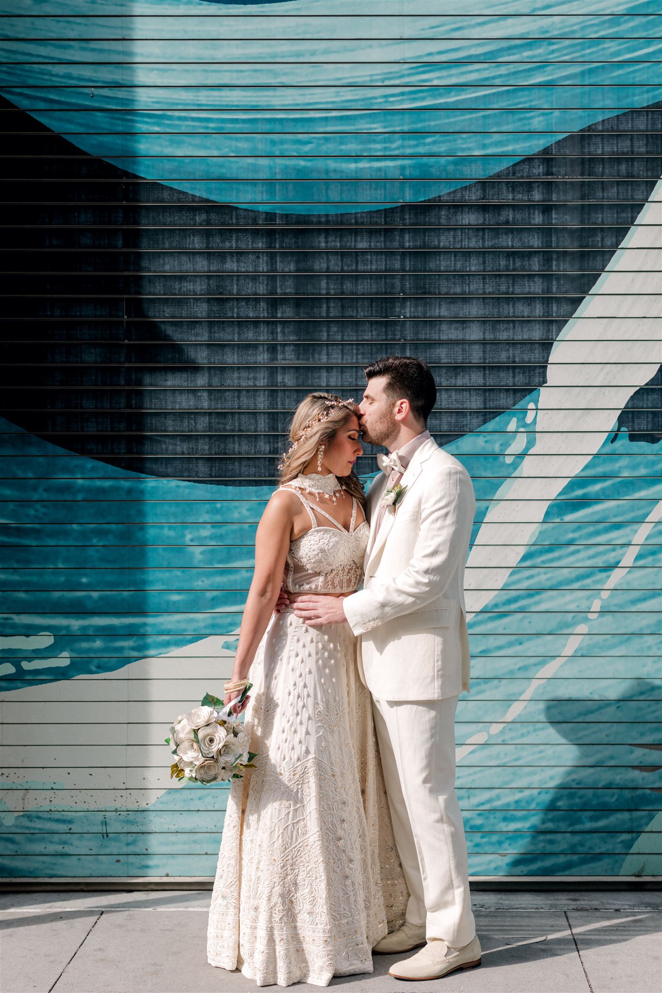 Bride and groom in white embracing in front of a colorful mural in New York City on their wedding day