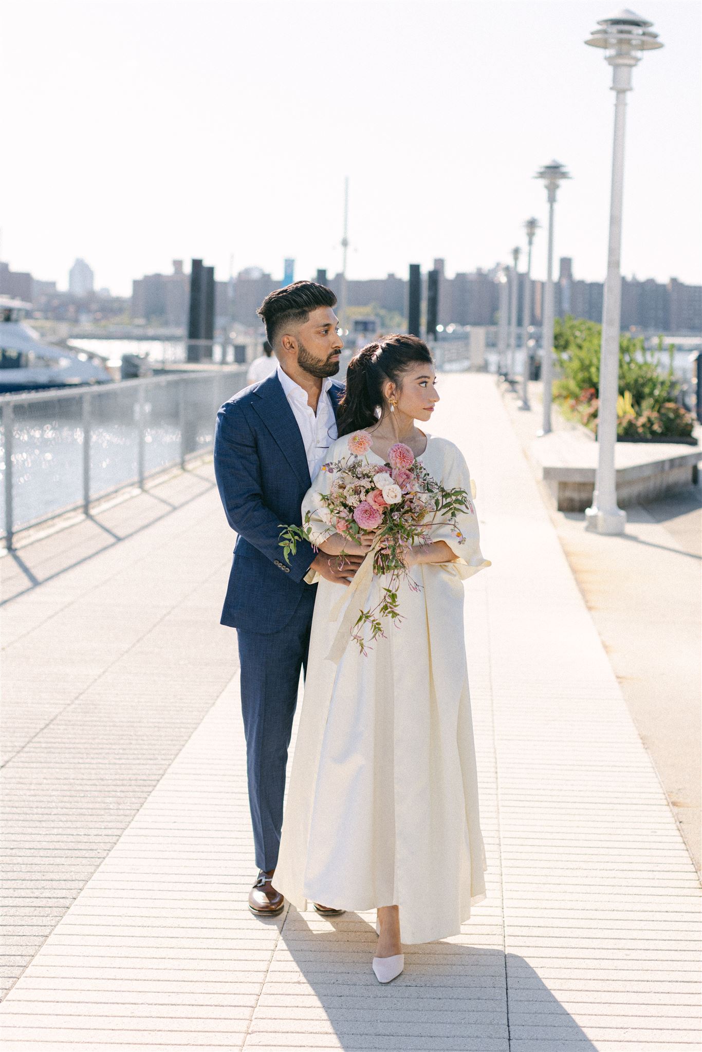 bride and groom wearing their wedding attire out by the river, the bride is holding a pink bouquet of flowers
