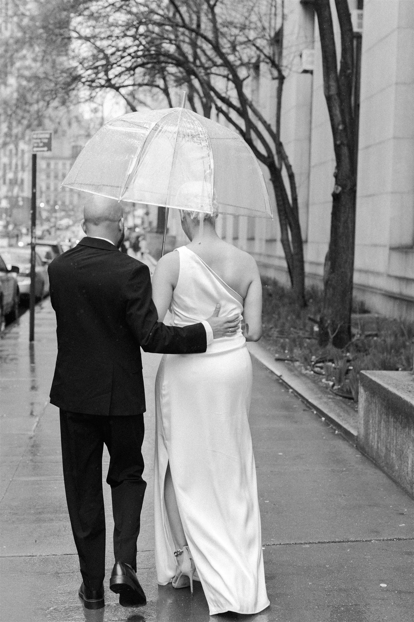 bride and groom walking underneath a clear umbrella after they got married at NYC city hall