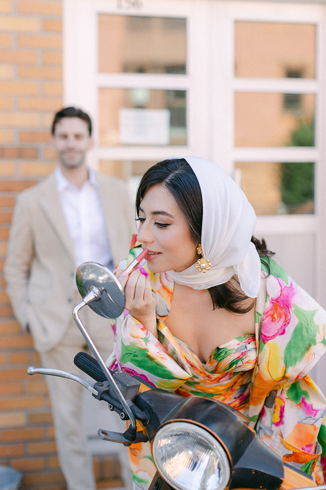 A woman putting on lipstick wearing a colorful dress and a scarf on her head