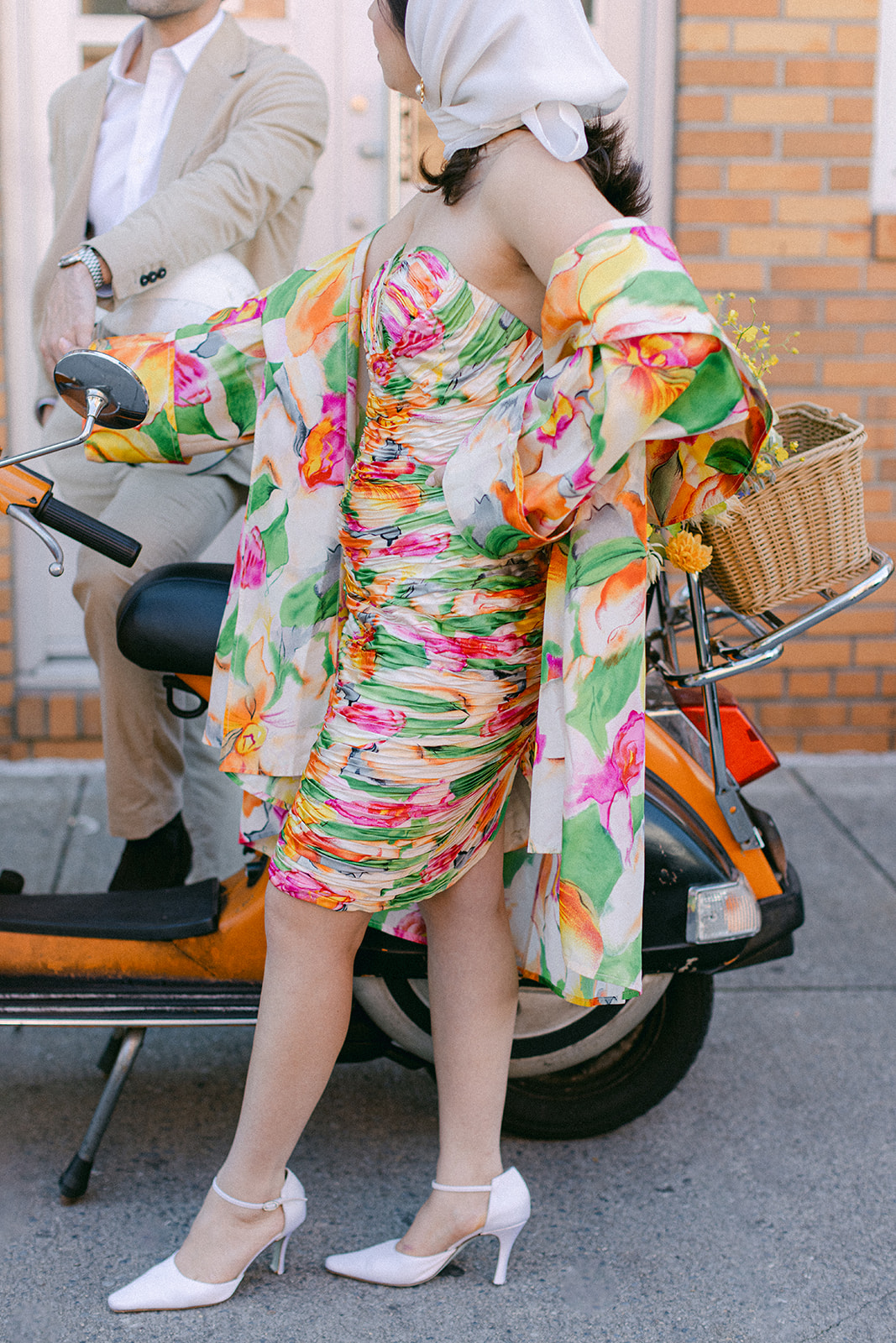 A woman wearing a colorful dress standing next to a moped in NYC