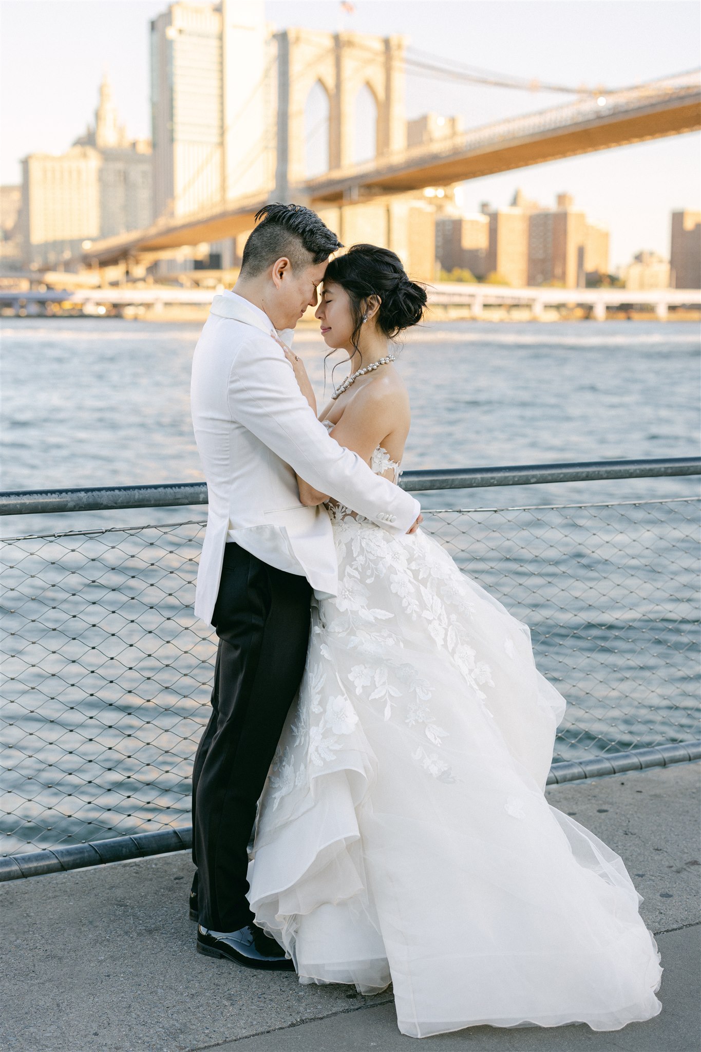 A wedding couple embracing in front of the brooklyn bridge in NYC