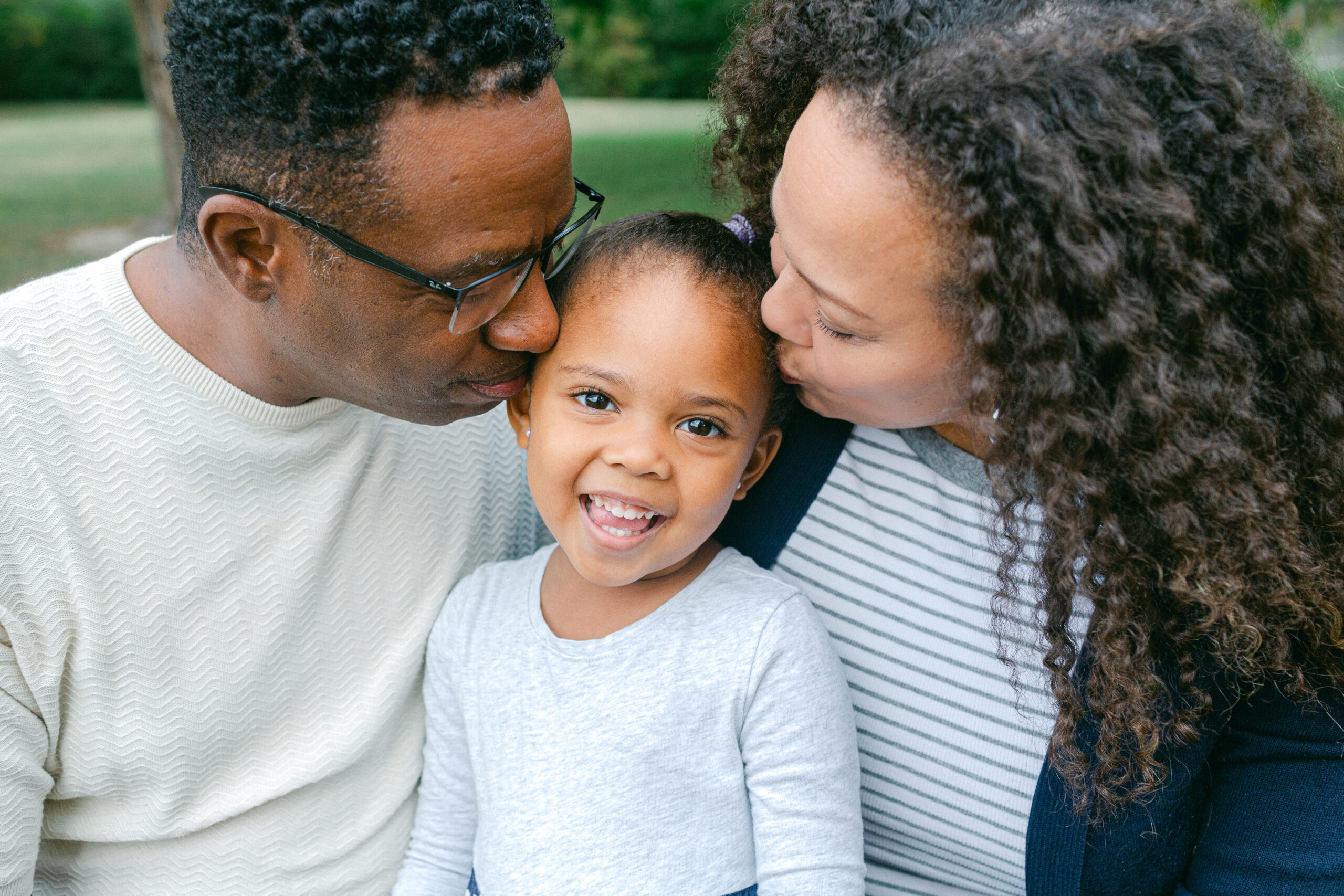 A mother and father kissing their daughter on the head