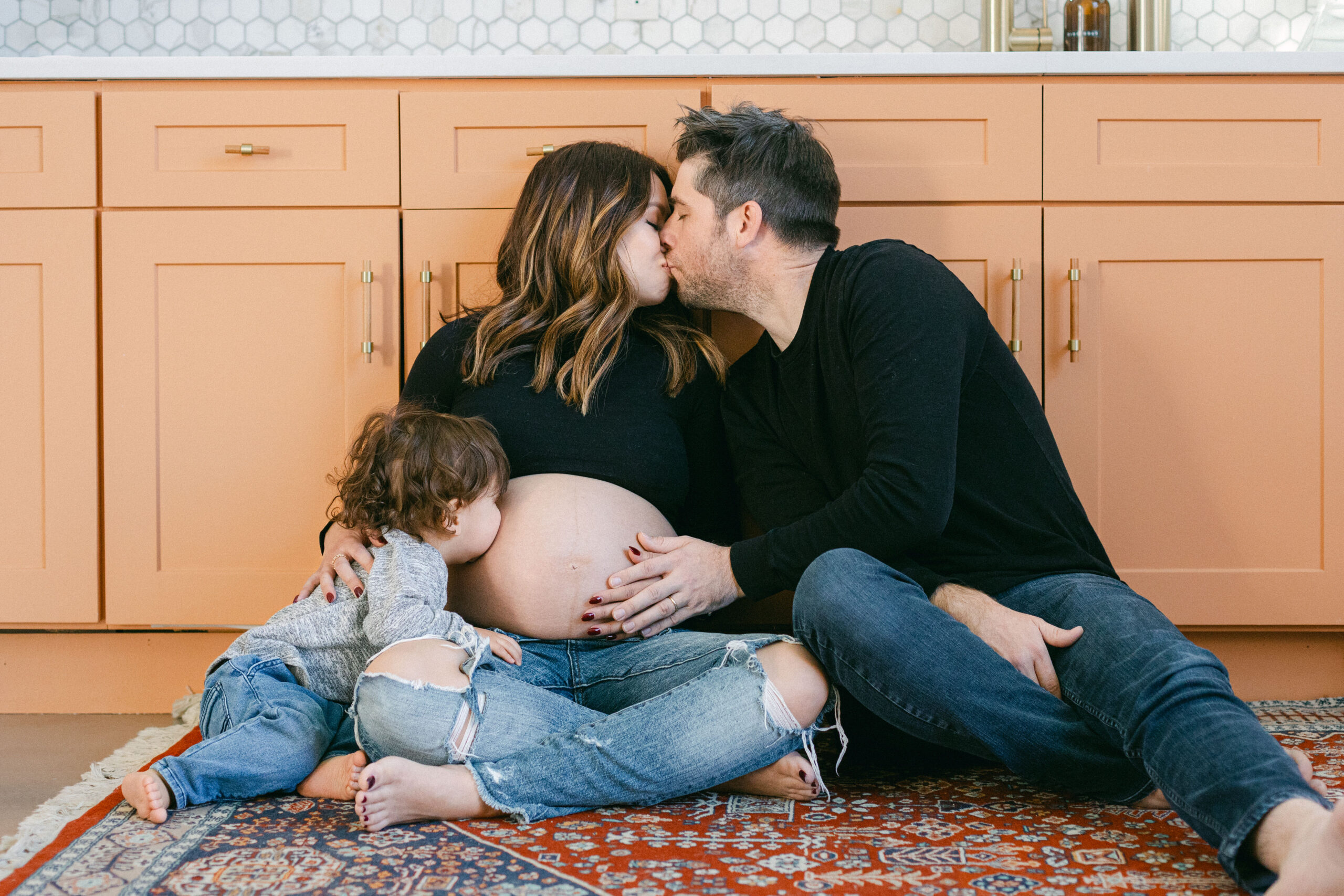 A husband kissing his pregnant wife while their toddler kisses her belly