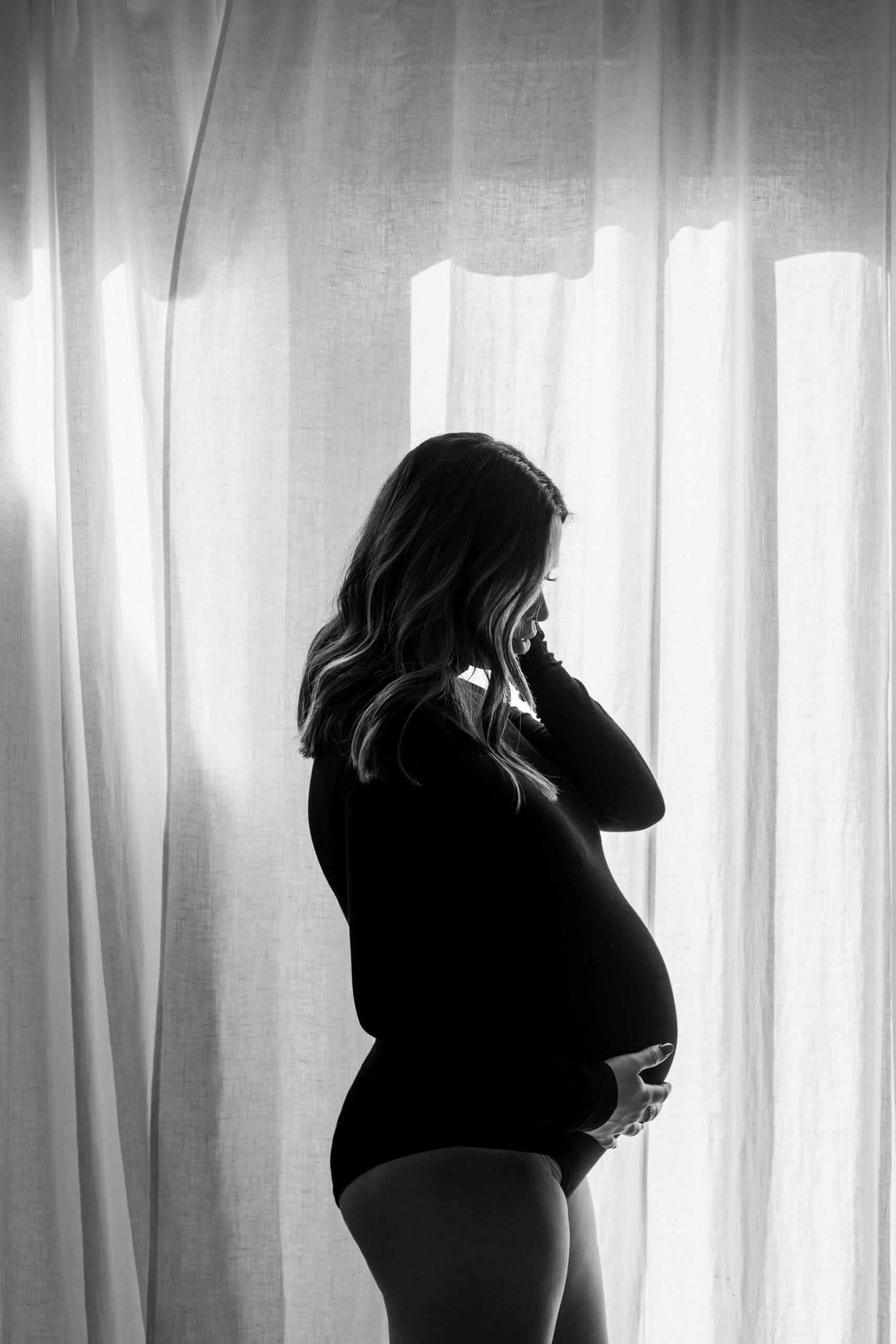 A black and white maternity photo in front of a window