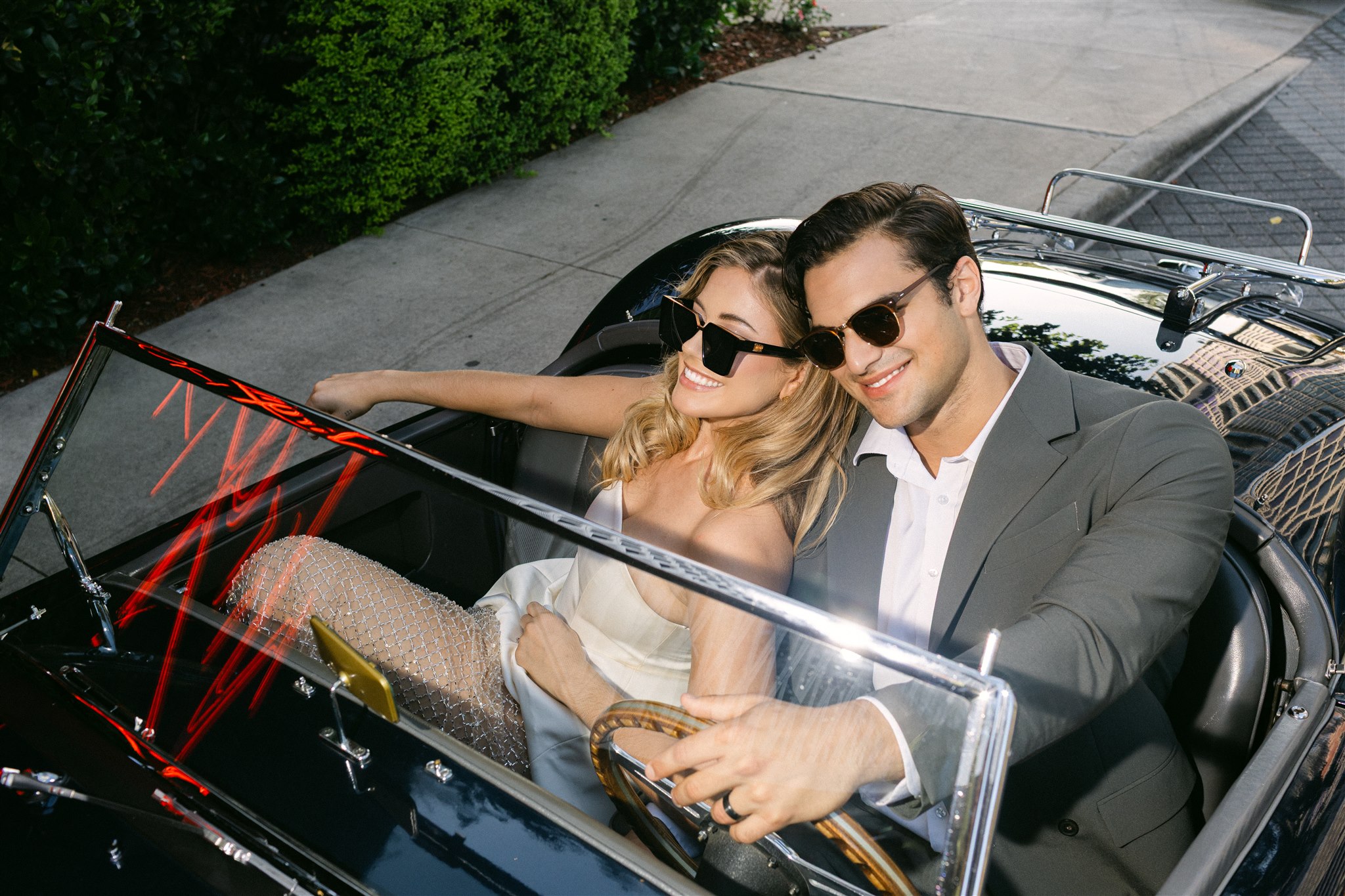A couple in a vintage getaway car in front of the virgin hotels dallas smiling 