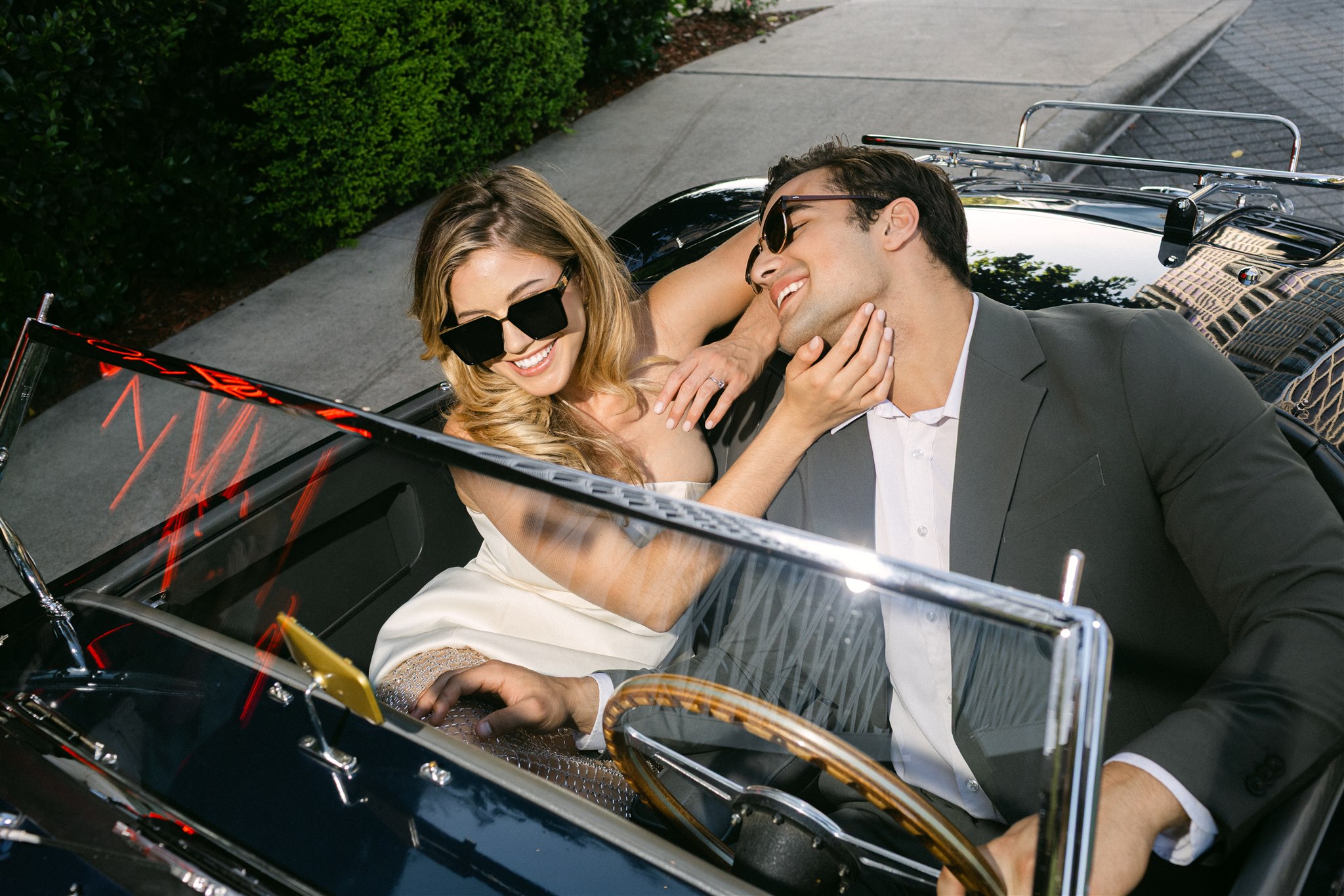 A couple in a vintage getaway car in front of the virgin hotels dallas smiling 