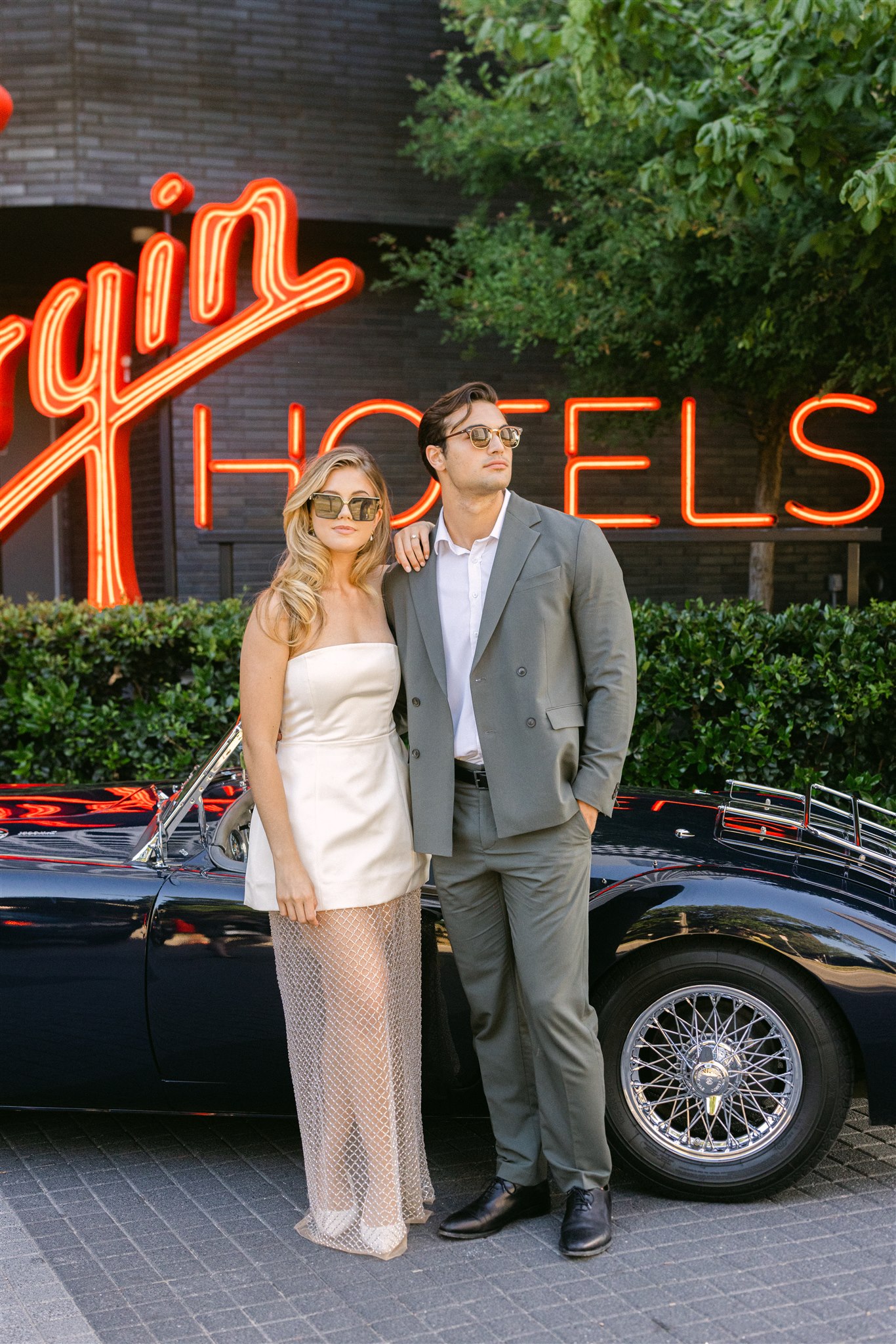 a bride and groom posing in front of a vintage getaway car at virgin hotels dallas