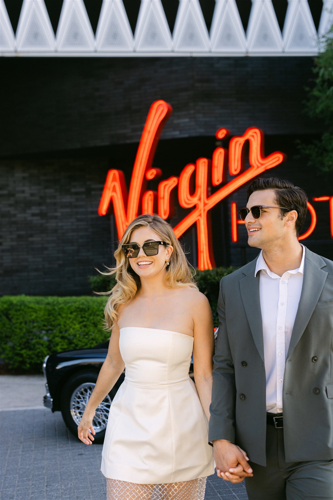 a couple walking hand in hand in front of the virgin hotels dallas sign during their rehearsal dinner