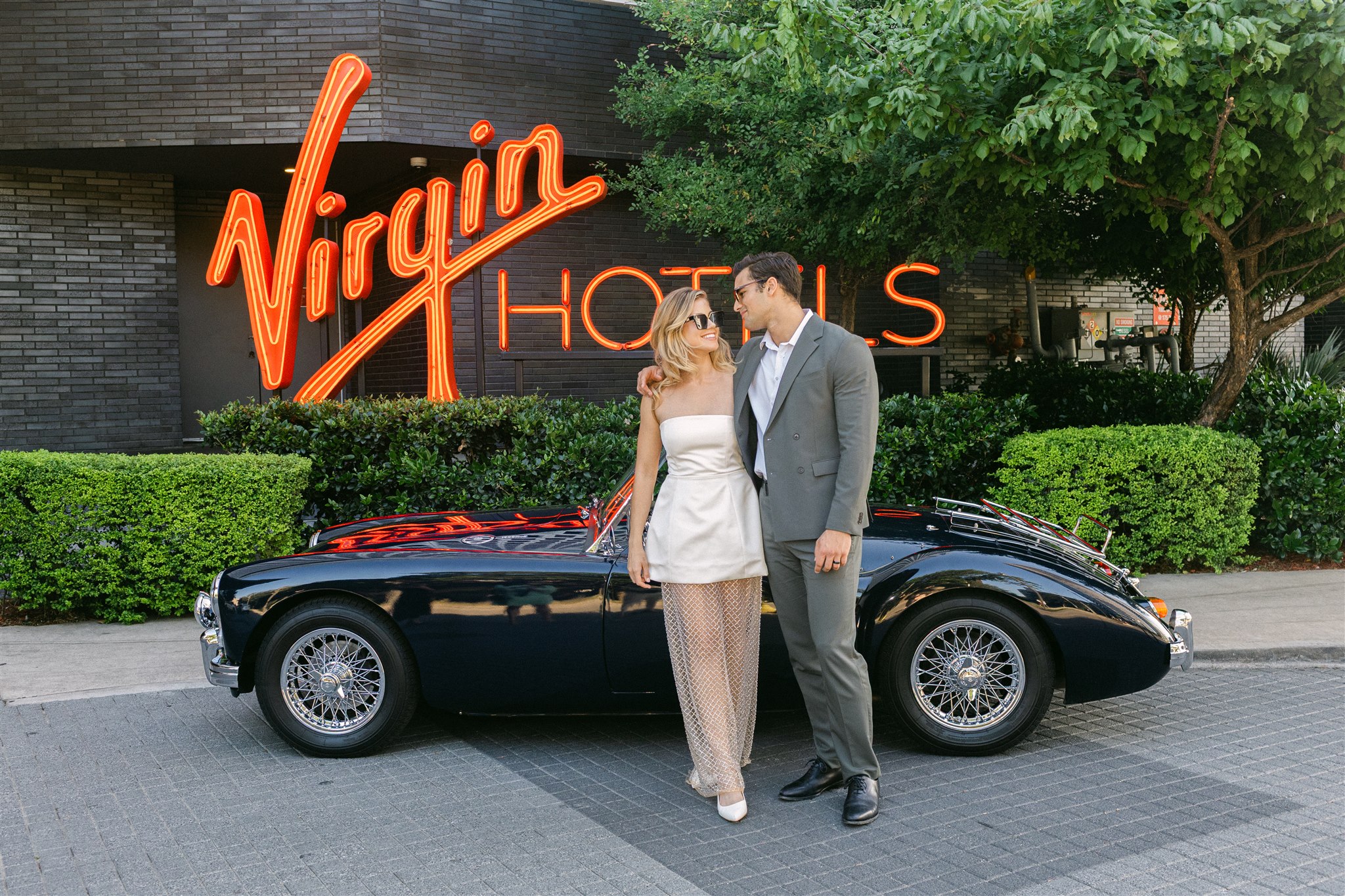a bride and groom posing in front of a vintage getaway car at virgin hotels dallas