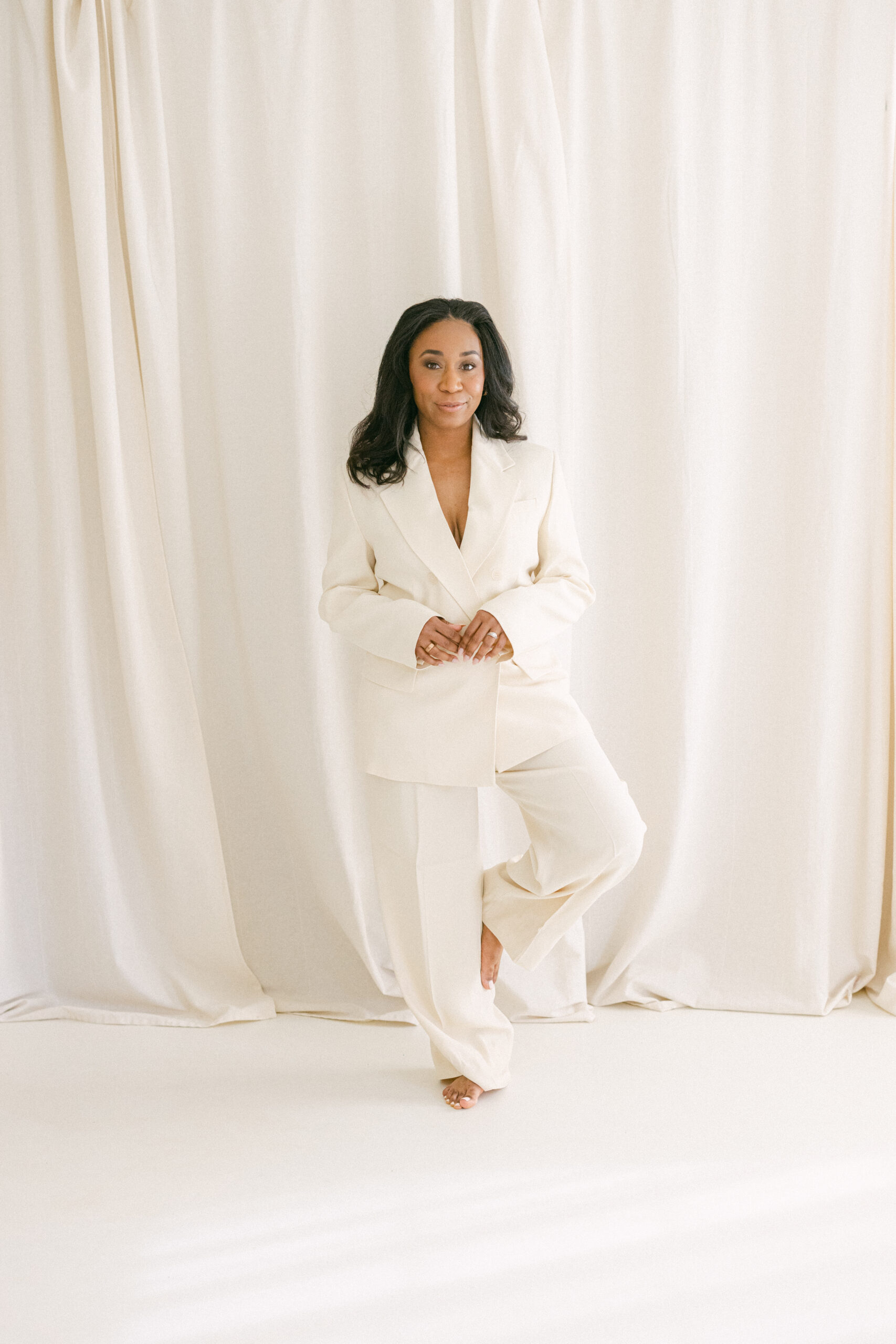 a woman wearing a cream suit standing in front of cream curtains