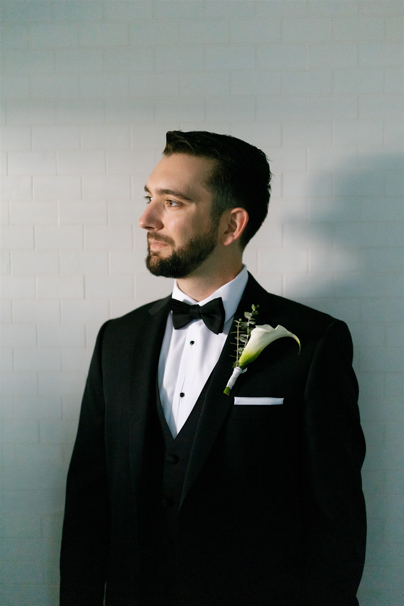 a groom wearing a black tux standing in front of a brick wall