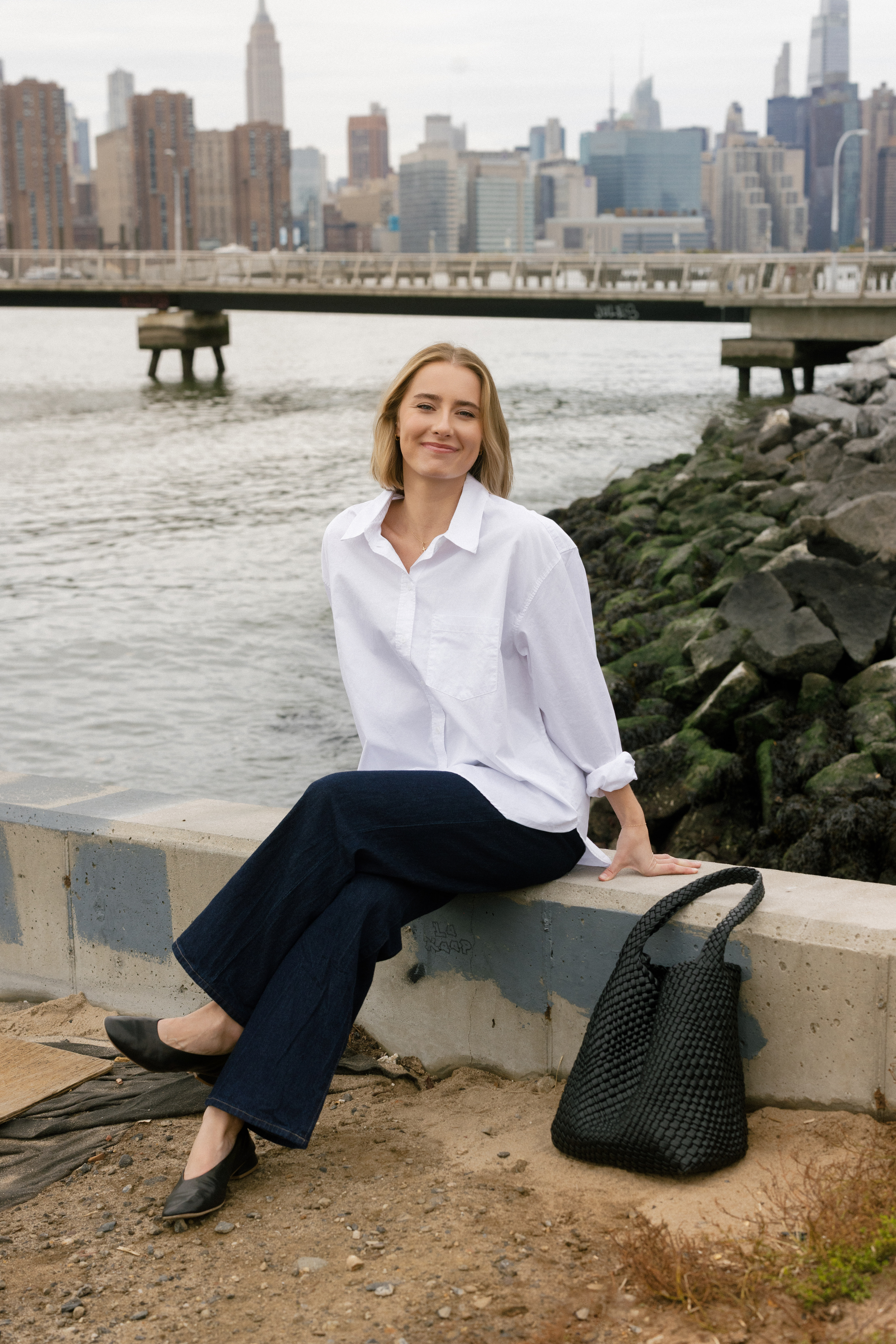 a girl wearing a white button down in front of the ocean with nyc skyline in the background