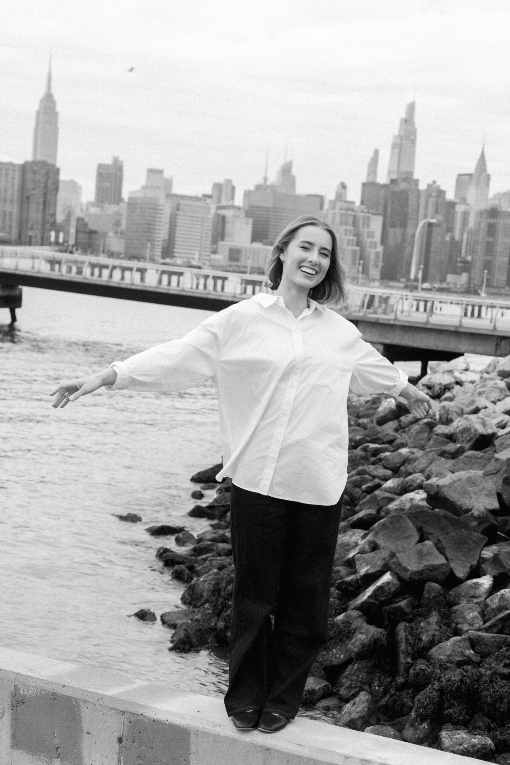 a girl wearing a white button down in front of the ocean with nyc skyline in the background