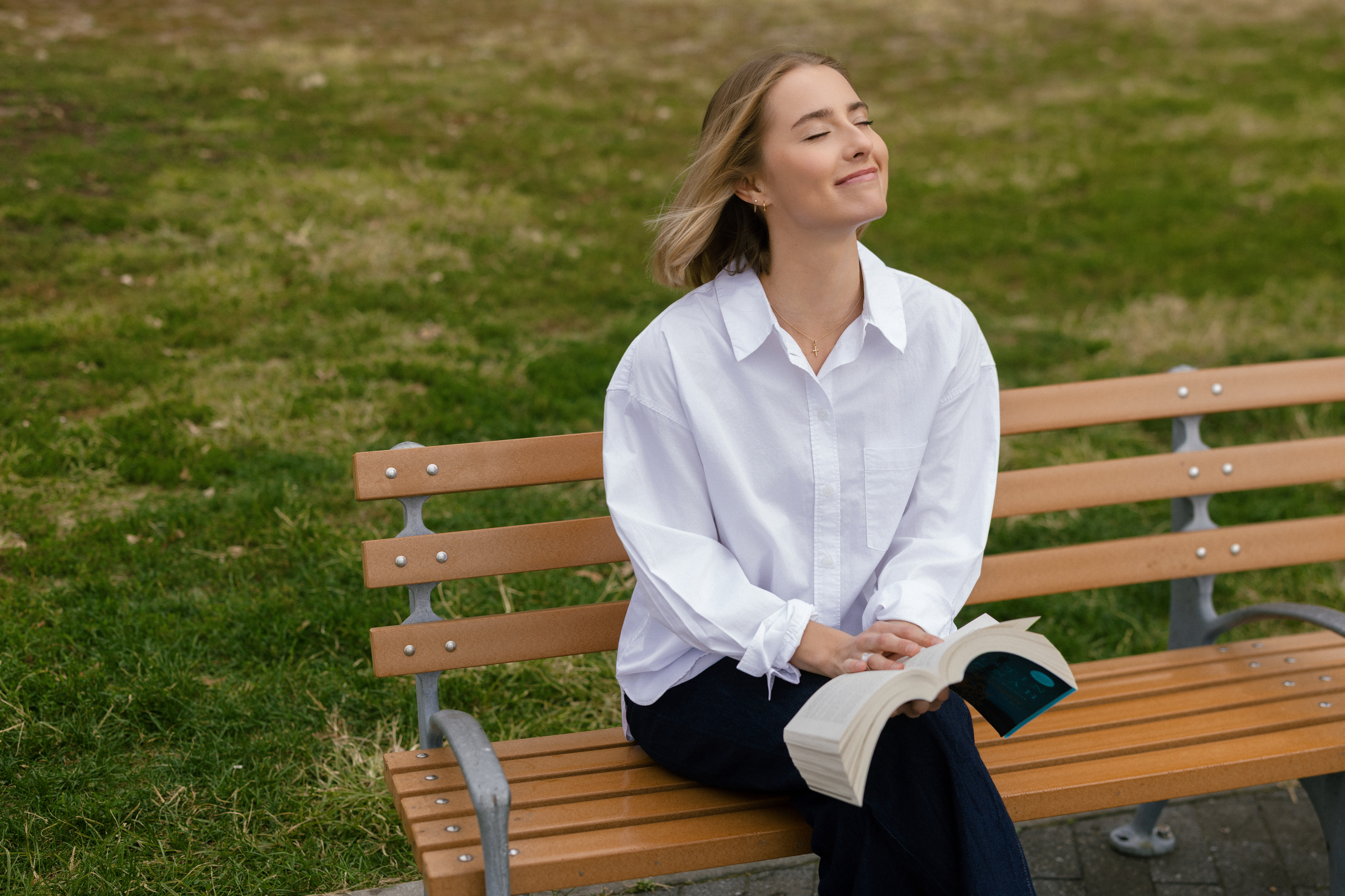 a girl wearing a white button down reading on a park bench in NYC