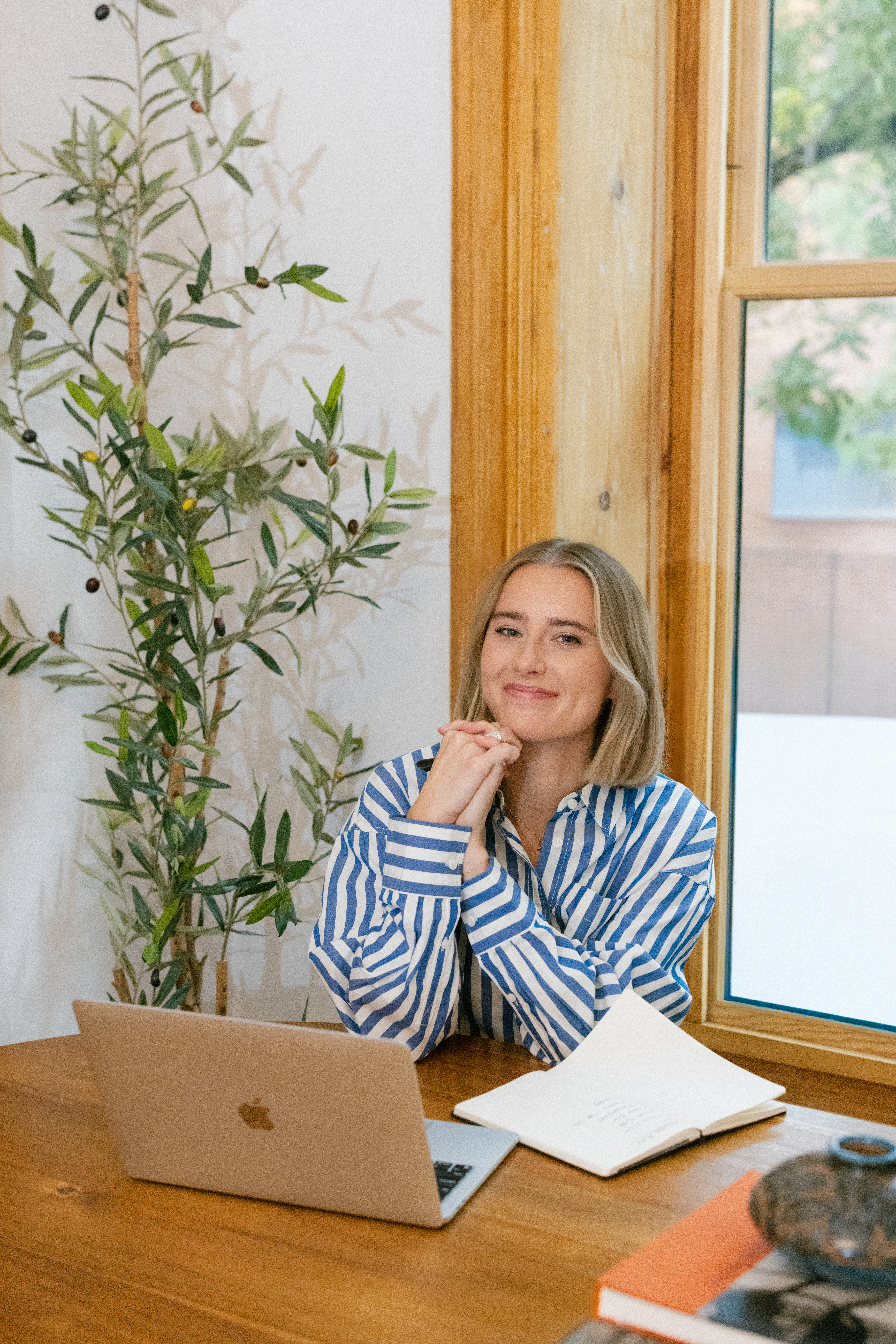 a girl wearing a blue and white stripped shirt working on her laptop for her brand photos