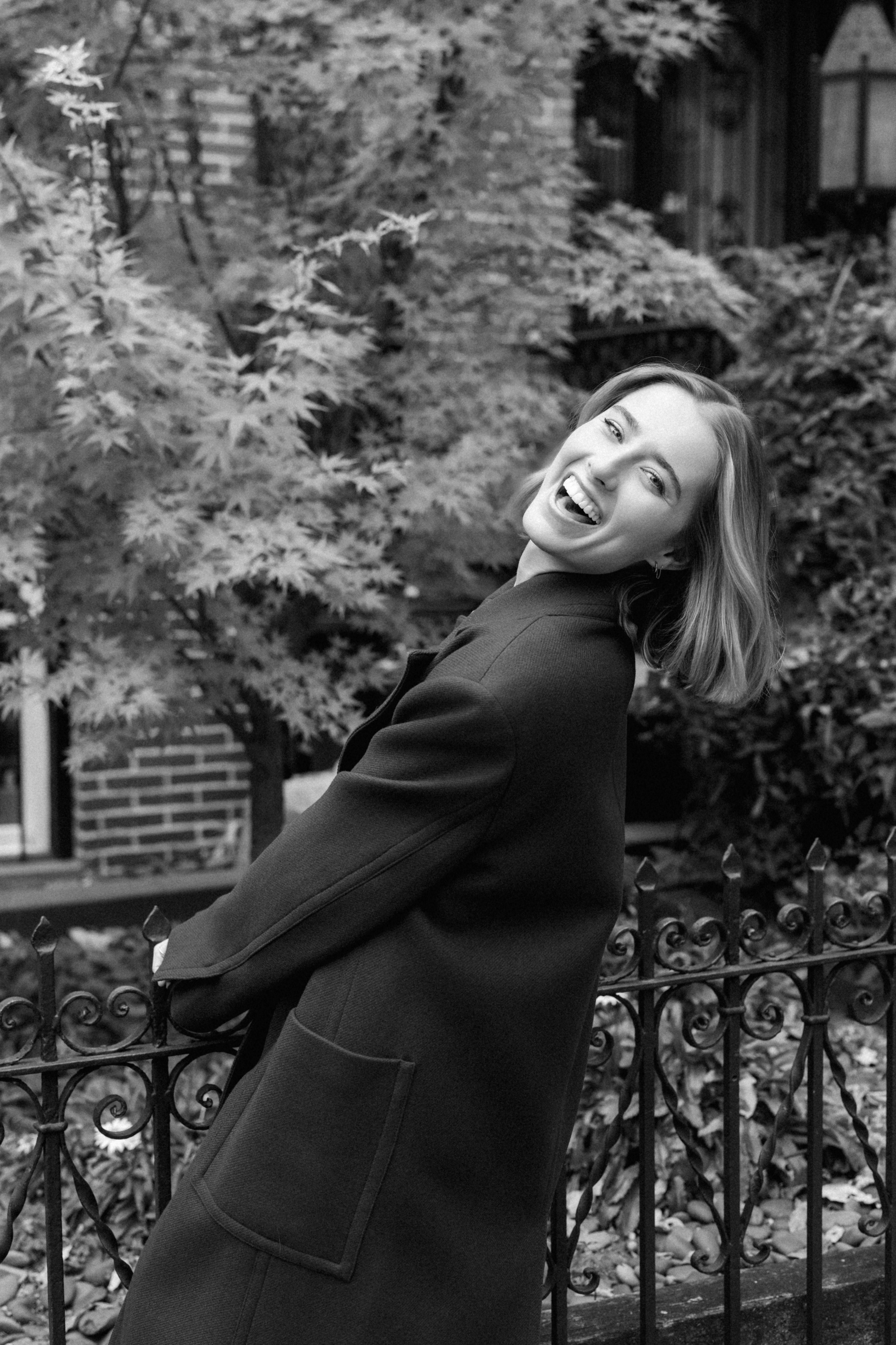 a girl wearing an olive green trench coat walking across the street in nyc