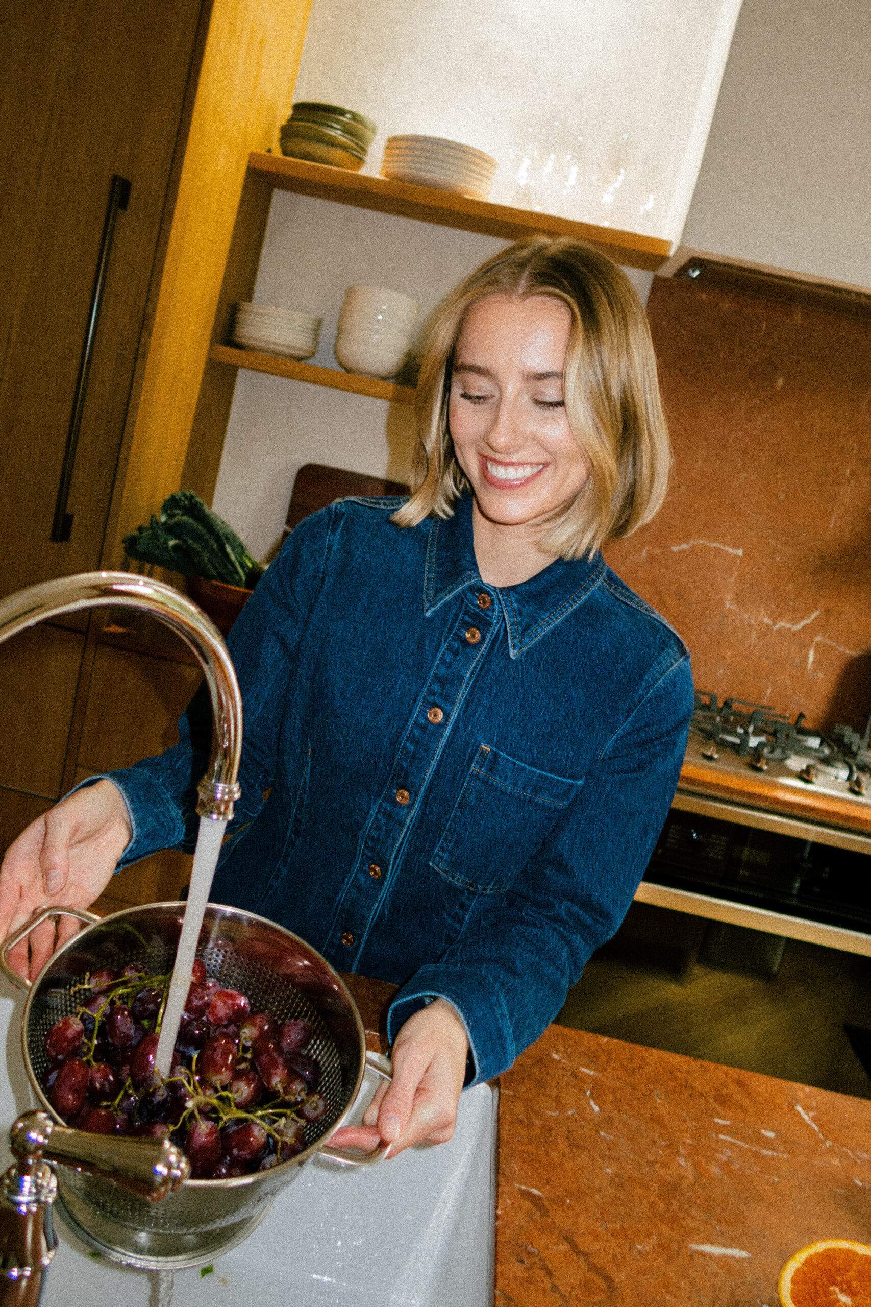a girl wearing all denim for her brand photos washing grapes in the kitchen