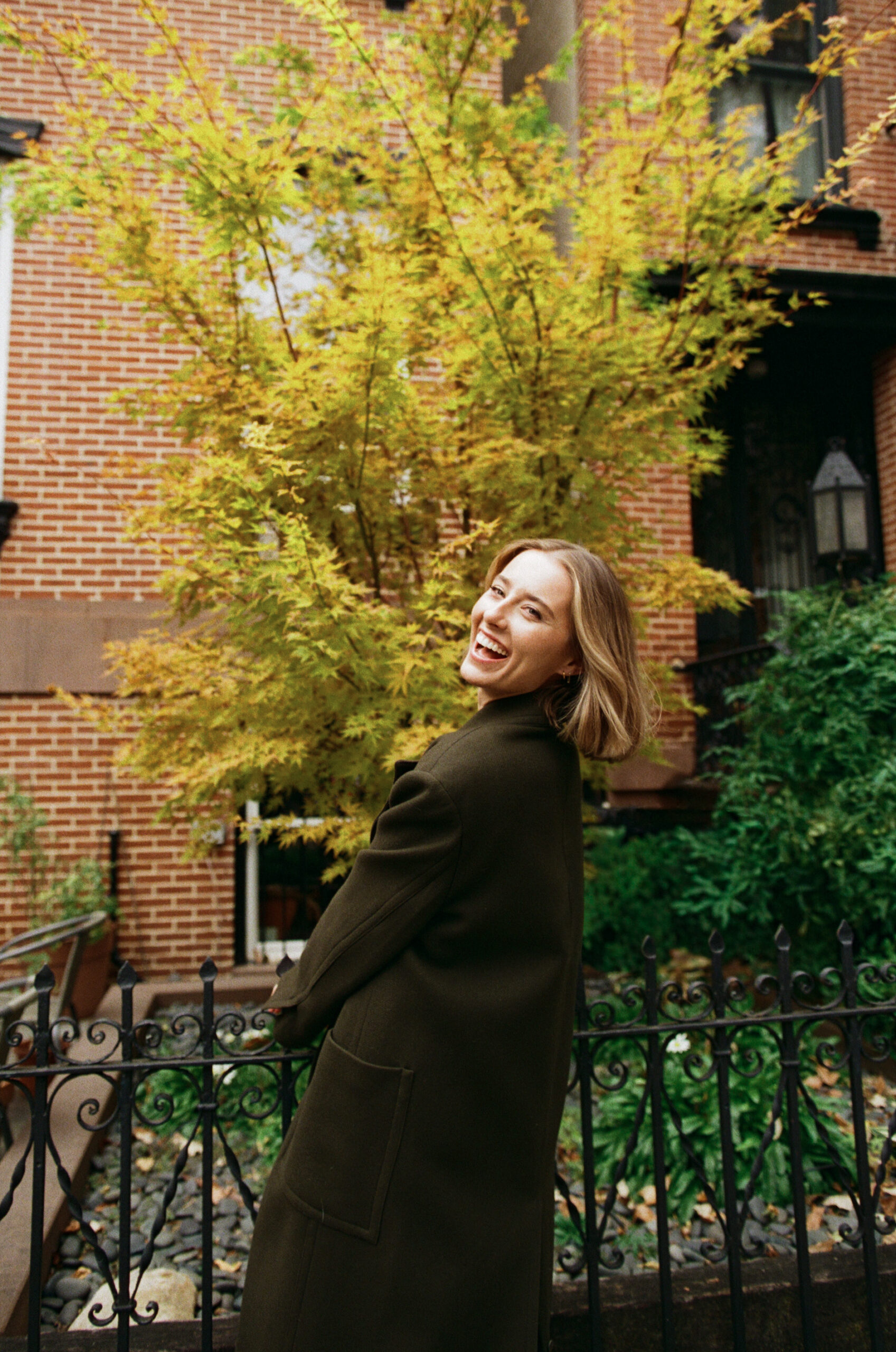 a girl wearing an olive green trench coat walking across the street in nyc